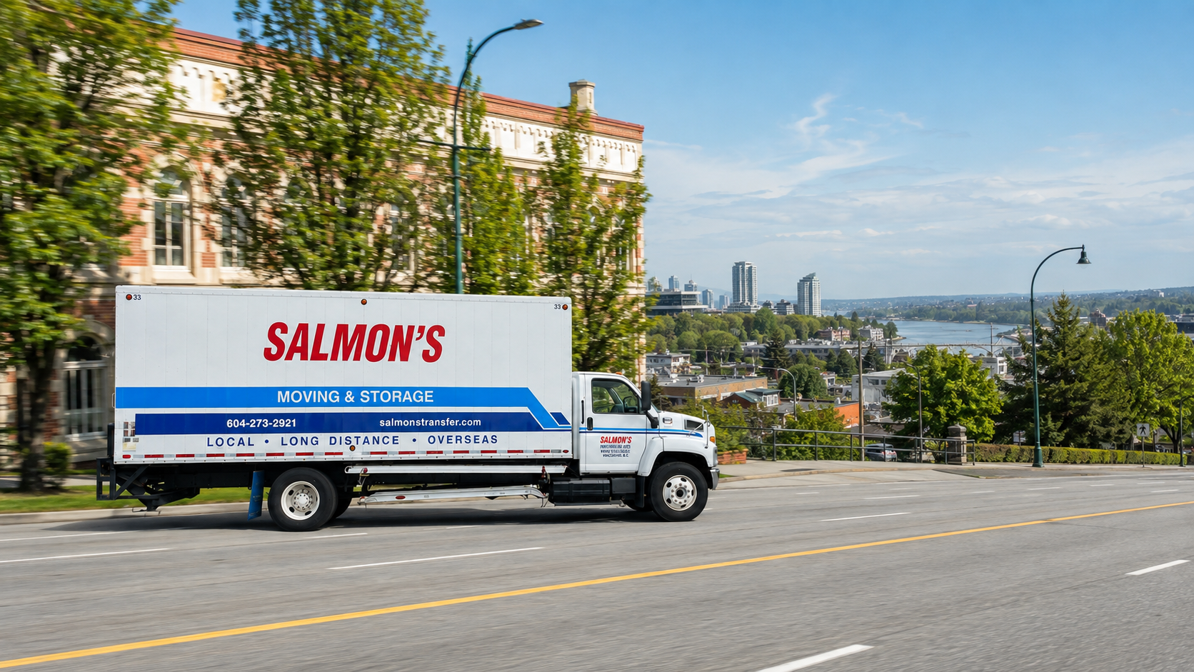 Salmon's Moving & Storage truck driving past heritage buildings in New Westminster with the Fraser River behind